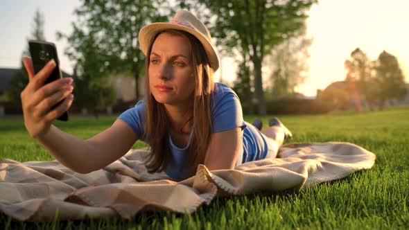 Girl Making a Selfie Lying Down on a Blanket in the Park at Sunset
