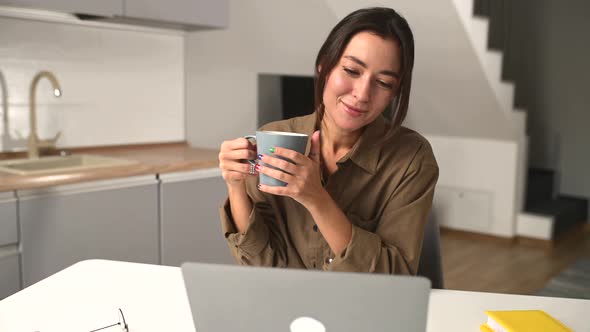 Relaxed Asian Multiracial Female Freelancer Relaxing Sitting with Cup of Coffee in Front of Laptop alt