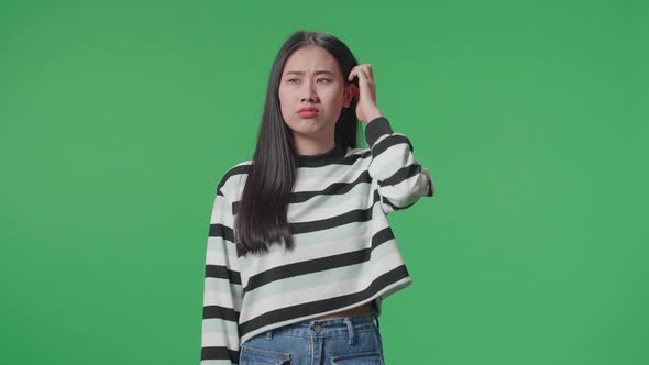 A Puzzled Asian Woman Is Standing In Front Of Green Screen Background