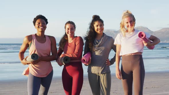 Portrait of group of diverse female friends holding yoga mats at the beach