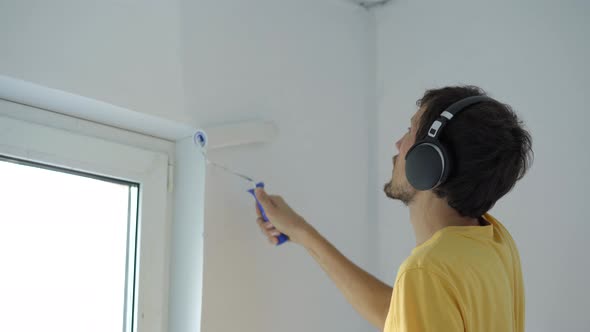 A Man Wearing a Yellow Tshirt Paints the Wall Using a Roller Painter