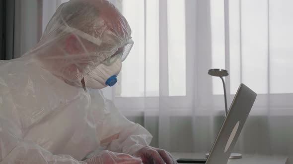 Concentrated Virologist Wearing Protective Suit Working with Laptop