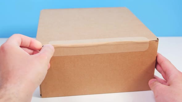 Close Up Man Hand's Opening Cardboard Box Package By Pulling Tear Tape