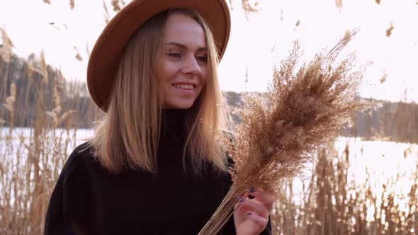 European Blonde Woman Blowing on Pampas Grass with Beige Hat in Black Sweater in the Countryside