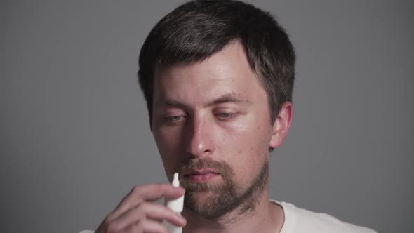 Young Caucasian Man Sprinkles Medicine for Rhinitis, Colds and Allergies Into His Nose From a White