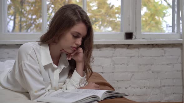 Young Attractive Woman Reads a Book on the Bed