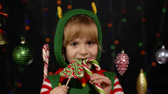 Child Kid Girl in Christmas Elf Santa Claus Helper Costume Licking Candy Lollipop Caramel Sweets