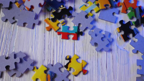 Close-up of the colorful puzzle pieces falling on the wooden background. Slow motion