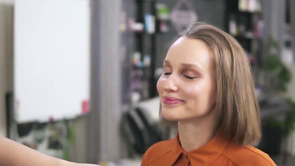 A Blonde is Sitting on the Chair and a Make Up Artist is Fihishing Her Visage with a Face Spray