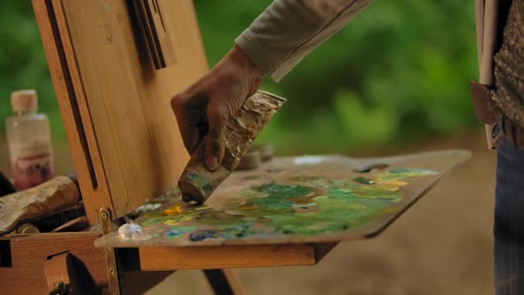 Woman Artist Squeezing a Tube with Yellow Orange Oil Paint on a Palette.