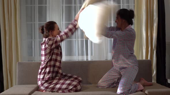 Two Sisters Twins Having Fun with Laugh and Smiles and Fighting with Pillows in the Evening