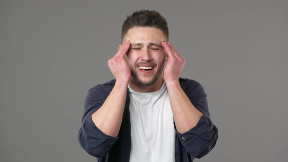 Portrait of Stressed Young Man in Casual Clothing Rubbing Temples Because of Headache and Suffering