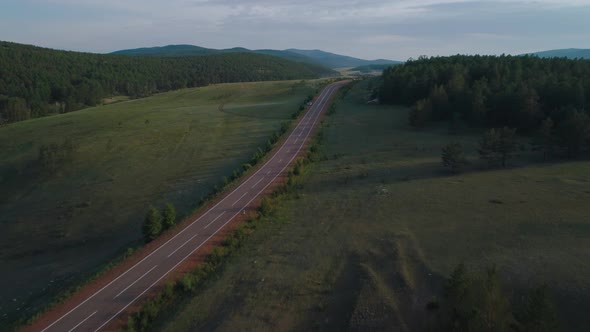 AERIAL, TOP DOWN: Dark Colored Car Driving Down an Asphalt Road Crossing the Vast Forest on a Sunny