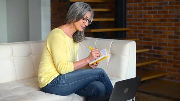 Mature Focused Woman Watching Online Webinars on the Laptop Sitting on the Sofa