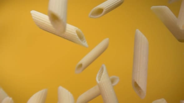 Closeup of the Pasta Penne Falling Down on a Yellow Background