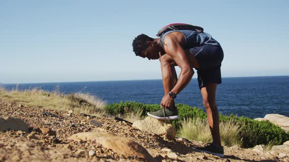 African american man exercising outdoors tying his shoe in countryside on a coast