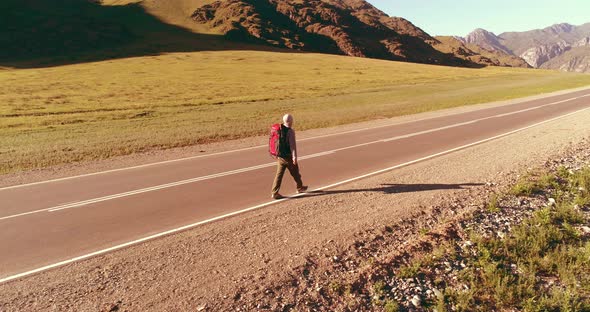 Flight Over Hitchhiker Tourist Walking on Asphalt Road, Huge Rural Valley at Summer Day, Backpack