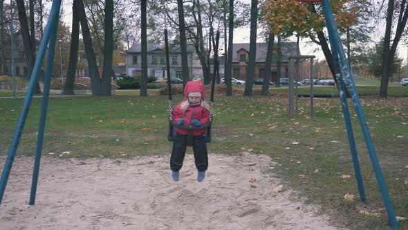 Girl is Swaying on Swing in Park at Autumn Day in Slow Motion