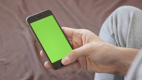 ZAJECAR, SERBIA - JANUARY 2017 Caucasian man rests in bed and holds greenscreen smart phone