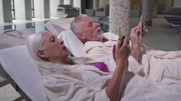 Happy Aging Couple Using Phones Relaxing in Hotel