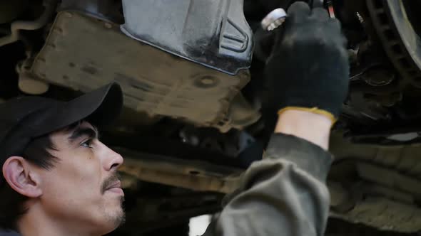 a Male Car Mechanic From Below the Car Tightens the Nut with a Wrench