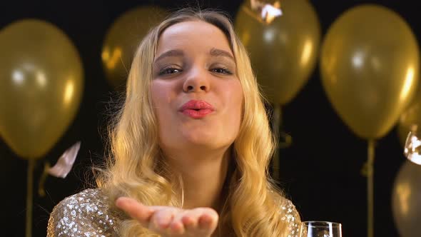 Cheerful Lady With Champagne Sending Air Kiss to Camera Under Falling Confetti