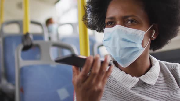 African american businesswoman with face mask talking on smartphone and sitting in bus