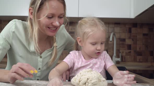 Mom and Daughter Cook Together at Home in the Kitchen and Knead the Dough