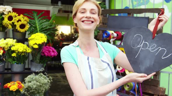 Smiling florist holding open sign on slate in flower shop