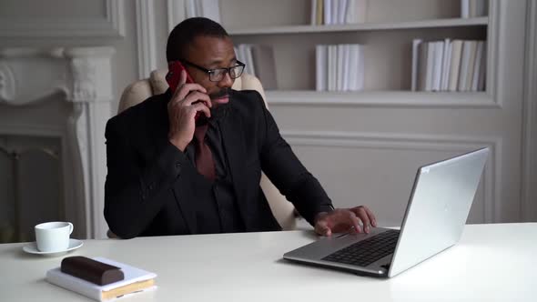 African-American Bearded Man in a Black Suit, Shirt, Stylish Glasses. A Businessman Is Working on a