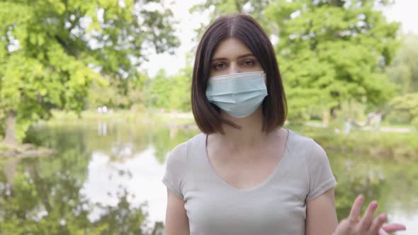 A Young Caucasian Woman in a Face Mask Talks to the Camera and Acts Frustrated in a Park