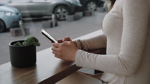 Young Woman Using Smartphone Sitting in Cafe Near the Big Window and Watching City Life