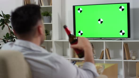 Man Drinking Beer and Eating Chips while Watching Green Screen TV at Home