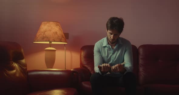 Young guy with shirt reads a book sitting in the living room at home