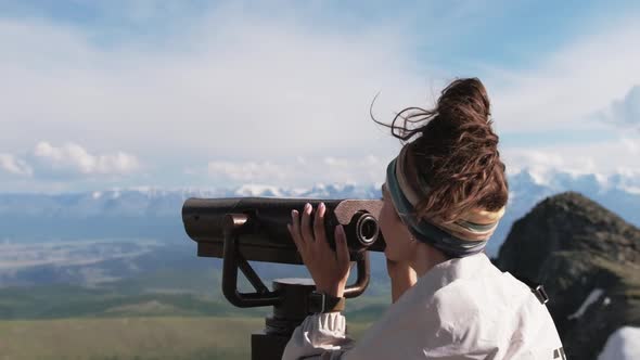 Attractive Girl Tourist on the Observation Deck Looks at the Mountains Through Binoculars