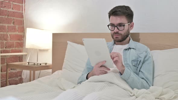 Focused Young Male Designer Using Tablet in Bed