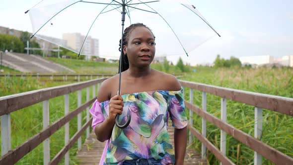 African-American Girl with Umbrella Walks Along Bridge