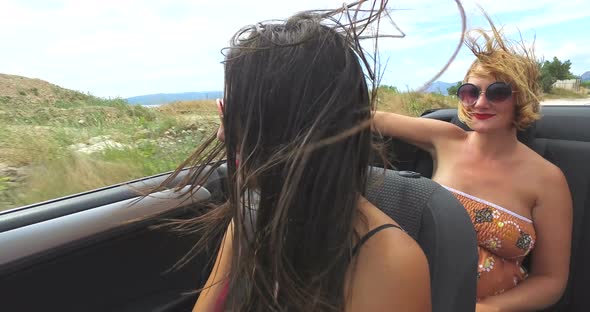 Two attractive women riding in cabriolet along dalmatian coast