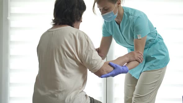 Doctor or Nurse is Helping an Elderly Woman to Get to Her Feet