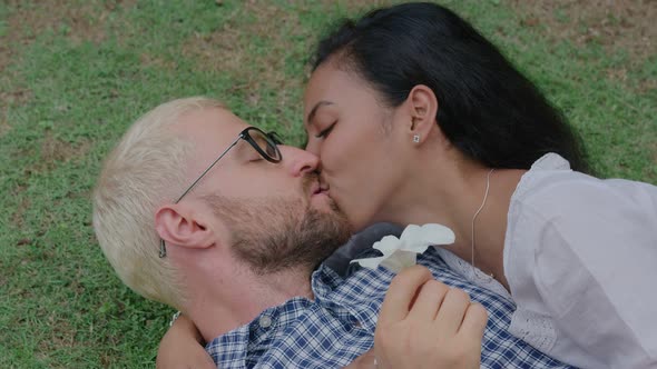 Young International Interracial Couple in Love Lying and Kissing on the Grass on a Sunny Day in a