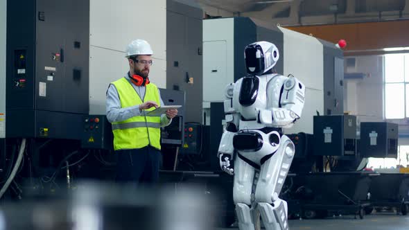 Man in Workwear Is Operating a Robot with a Tablet