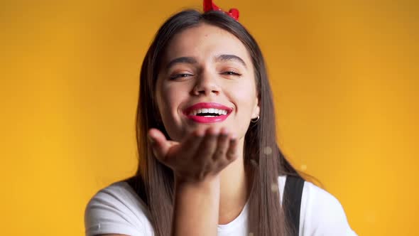 Attractive Girl Blowing Shiny Dust or Sparkles Confetti on Yellow in Studio