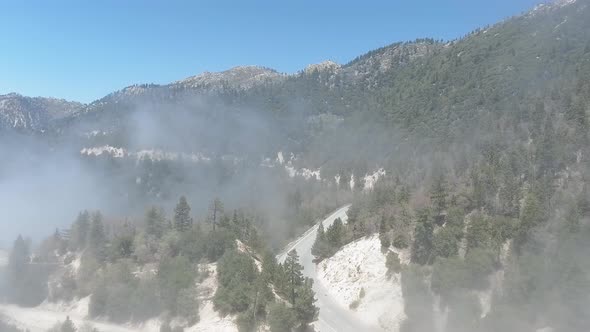 Drone bird's-eye view of a foggy road winding through forest hills in California, USA