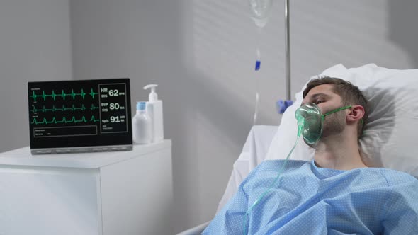 The Man Lies on the Bed in the Hospital in Oxygen Masks and Regains Consciousness