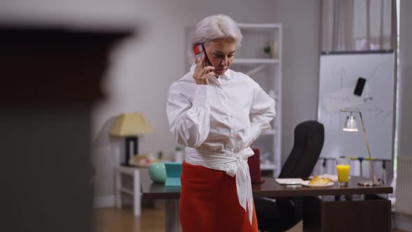 Greyhaired Successful Businesswoman Talking on Phone Walking Side to Side in Office in Slow Motion