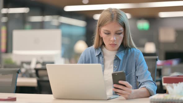 Young Woman Using Smartphone While Working on Laptop