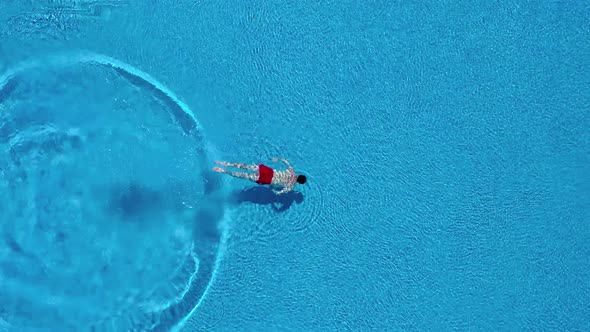 View From the Top As a Man Dives Into the Pool and Swims Under the Water