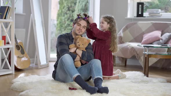 Wide Shot Portrait of Patient Young Man Sitting on Soft Carpet in Living Room As Playful Cute Girl