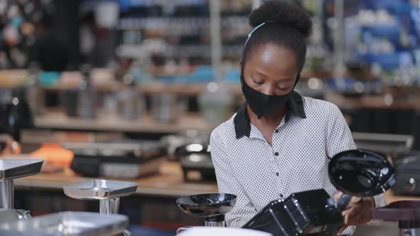 Young Black Woman with Face Mask is Shopping in Hardware Store Choosing Home Appliances Viewing