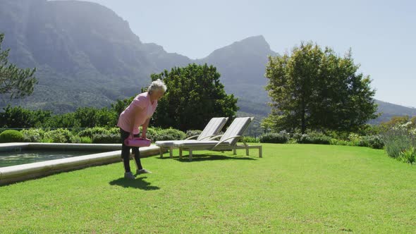 Caucasian senior exercising laying out a yoga mat in garden in the sun